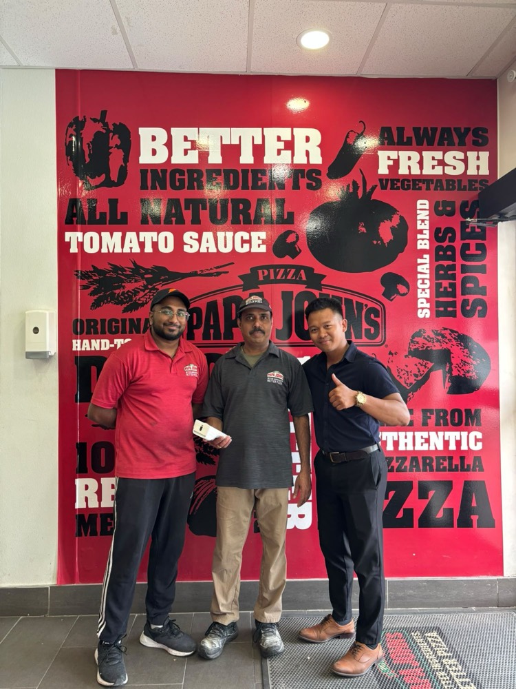 GT Payments rep with the Papa John’s team in front of the store’s branded wall, holding their new Clover terminal